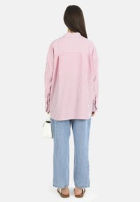 Camisa de rayas rojas y blancas de gran tamaño con mangas largas, combinada con jeans rectos de color azul claro y accesorios como un bolso blanco.