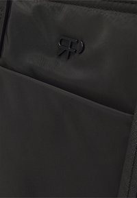 Gros plan d'un tissu noir avec un logo noir en relief présentant une lettre R imbriquée et un design R en miroir.