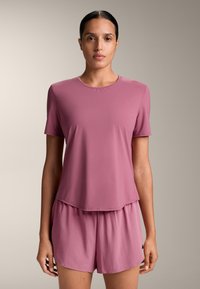 Světle růžový krátký rukávový top s kulatým výstřihem a volným střihem, doplněný o volné kraťasy ve stejném odstínu. Obě kusy jsou vyrobeny z hladkého, lehkého materiálu.