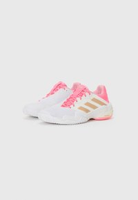 Zapatillas deportivas blancas con acentos en rosa, con una parte superior texturizada, tres rayas beige y un patrón de agarre pronunciado en la suela.