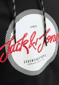 Sort hættebluse med et stort hvidt cirkulært logo og røde tekst "Jack & Jones" samt stribede sort og hvide detaljer. Justerbare snore.