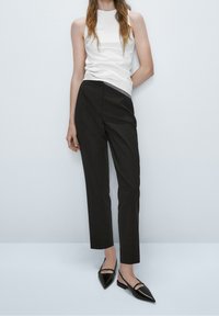 Biała bezrękawnik w połączeniu z dopasowanymi czarnymi spodniami i czarnymi, spiczastymi balerinami. Strój charakteryzuje się gładkimi fakturami i dopasowanym krojem.