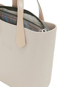 Béžová gumová kabelka se strukturovaným tvarem a dvěma plochými rukojeťmi. Interiér obsahuje zipovou zelenou tašku s podšívkou z kostkované látky.