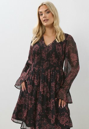 Robe noire à motifs floraux comprenant un corsage cintré, un texture smockée et des manches cloche transparentes. Le tissu présente un motif de roses dans des tons bordeaux.
