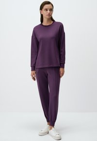 Felpa viola e pantaloni jogger abbinati in tessuto morbido e liscio; presenta polsini a costine e una vestibilità rilassata con aperture per le caviglie elasticizzate.