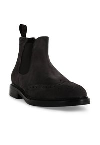 Stivaletto Chelsea in suede nero con pannelli laterali elastici, dettagli brogue, suola piatta e laccio sul retro per una facile calzata.