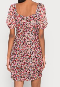 Robe mini à fleurs avec des manches courtes bouffantes. Fabriquée en tissu léger, dotée d'un design smocké dans des teintes rose, orange et noire. Encolure carrée dans le dos.