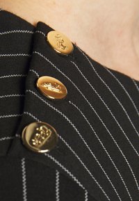 Černá látka s proužkem a třemi lesklými zlatými knoflíky, každý s vyraženými různými symboly v královském stylu.