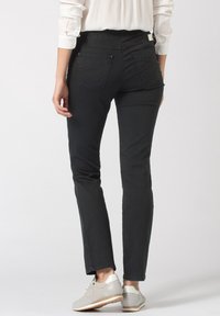 Jeans negros de corte slim, material elástico, diseño de cinco bolsillos y detalles de costura sutiles. Combinados con zapatillas de malla gris claro.