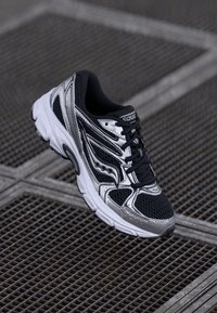 Black and silver running shoe with a mesh upper, curved design, textured accents, and white sole, featuring contrasting colored stitching.