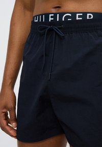 Μπλε ναυτικό μαγιό με κορδόνι και ελαστική μέση με λογότυπο. Λείο ύφασμα και ελαφρύ υλικό, κατάλληλο για χρήση στο νερό.