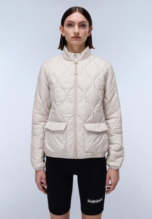 Beige gewatteerde jas met een hoge kraag en een rits aan de voorkant, met twee vo pockets en elastische manchetten, gedragen over zwarte shorts.