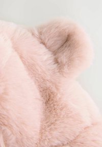 Tissu en fausse fourrure rose doux avec une texture pelucheuse, présentant des bords arrondis et des variations subtiles, mettant en avant un design confortable et accueillant.