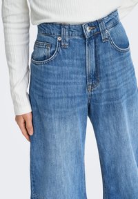 Ljusblå högmidjade jeans i denim med lös passform. De har fem fickor, knappstängning och kontrasterande sömmar.