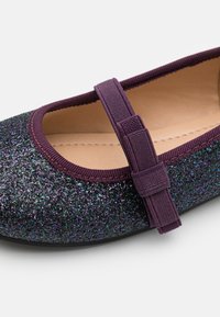 Glitzernde schwarze Ballerinas mit lila Elastikband und Besatz, ausgestattet mit einem glatten Innenfutter und einer strukturierten, glitzernden Oberfläche.