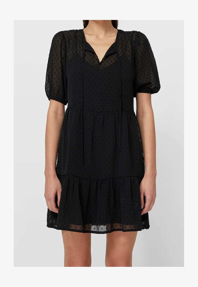 Robe noire en tissu transparent avec des pois texturés, manches courtes bouffantes, encolure en V, jupe à volants, et silhouette ample.