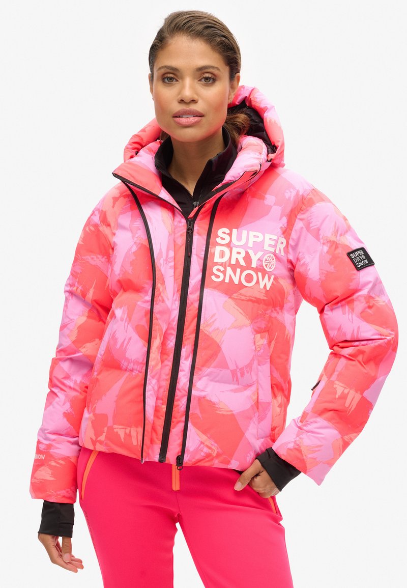 Veste rembourrée rose et corail avec un motif abstrait, zips noirs, col haut et impression de logo. Elle dispose d'une capuche et de poignets contrastants.
