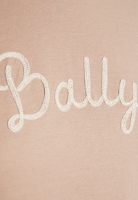 Gros plan sur un tissu beige avec le mot "Bally" brodé en lettres cursives tricotées blanches.
