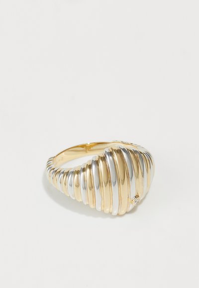 Gebogene Armreif mit abwechselnden gold- und silberfarbenen Metallbändern in einer glatten, strukturierten Oberfläche und einem kleinen Diamantakzent.