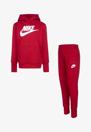 Hanorac roșu Nike cu o buzunare frontală și logo alb, asortat cu pantaloni de trening roșii, care prezintă un logo alb pe piciorul stâng. Material moale.