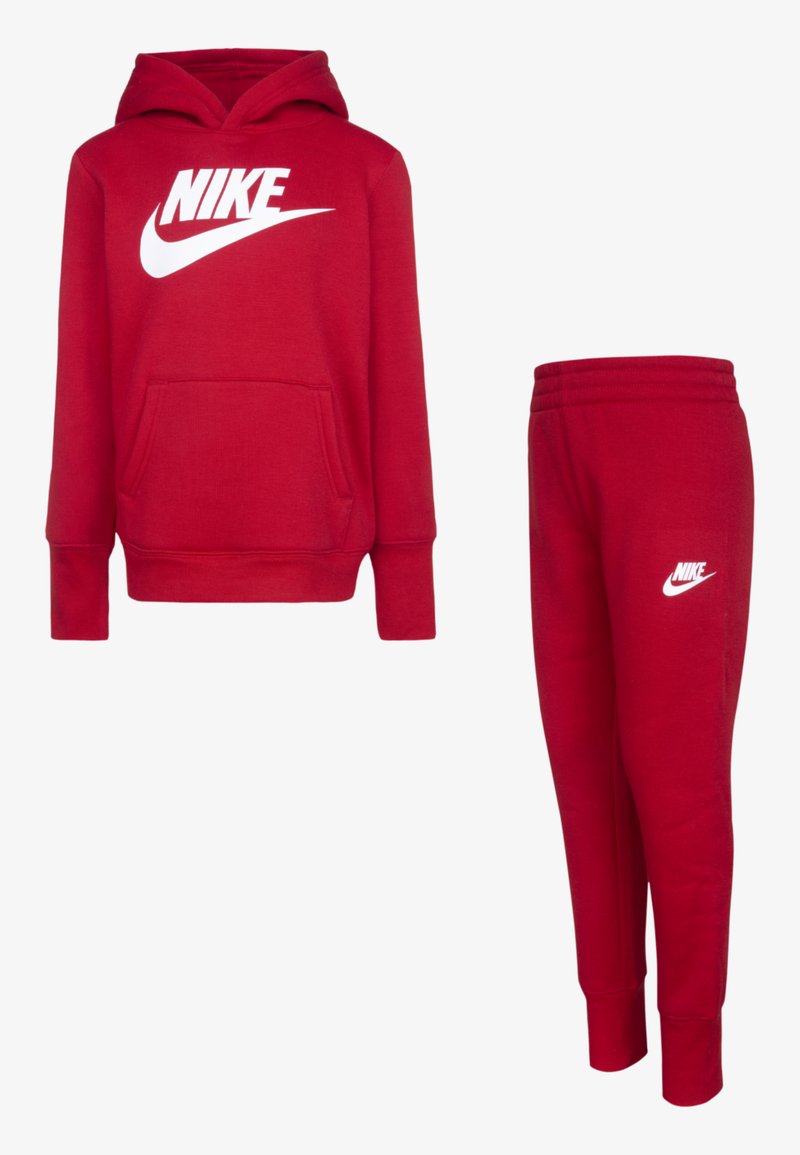 Piros Nike kapucnis pulóver elülső zsebbel és fehér logóval, párosítva egyező piros sportnadrággal, a bal lábon fehér logóval. Puha anyag.