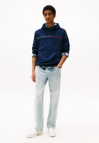 Marineblå hettegenser med horisontale striper, kombinert med lyseblå jeans og hvite joggesko. Uformell passform, laget av bomull.