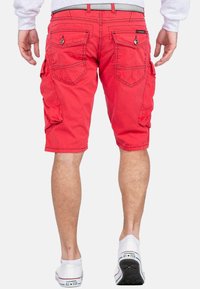 Rode cargoshorts met meerdere zakken, een relaxte pasvorm en een omgeslagen zoom. Het materiaal lijkt lichtgewicht met zichtbare stikseldetails.