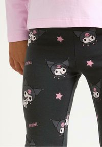 Sorte leggings med et gentagende mønster af en figur i sort outfit med pink accenter og stjerner, lavet af et blødt strækstof.