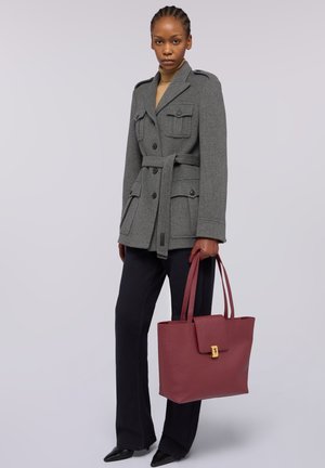 Grå uldjakke med fire lommer og et bælte, kombineret med sorte bukser. Holder en burgunderfarvet lædertaske med en guldlås.