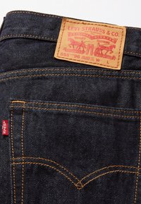 Poche arrière de jean en denim bleu foncé avec coutures orange et étiquette rouge Levi's, ornée d'un label en cuir marron clair de la marque Levi Strauss & Co.