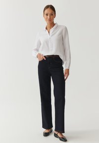 White long-sleeve shirt with button placket, paired with dark blue straight-leg jeans. Black flats complete the outfit.