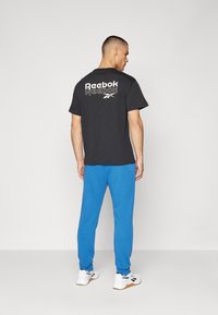 Melna kokvilnas T-kreklu ar balto "Reebok" logotipu uz aizmugures, apvienots ar ziliem treniņbiksēm un baltām kedām ar melniem akcentiem.