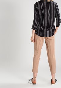Blouse rayée noir et blanc à manches trois-quarts, associée à un pantalon beige fuselé. Le mannequin porte des sandales à enfiler.