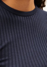 Gros plan sur une personne portant un haut en tricot côtelé bleu marine foncé avec un col rond.