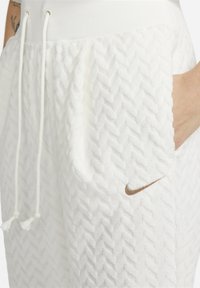 Vita texturerade joggers med en herringbone-design, dragsko i midjan, sidofickor och en liten bronzfärgad Nike-logotyp på vänster ficka.