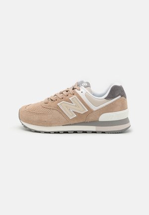 Baskets New Balance beige et blanches avec tige en daim, fermeture à lacets et semelle rembourrée, vues de côté sur fond blanc.