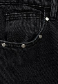 Gros plan sur une poche de jean en denim noir avec des rivets argentés et une boucle de ceinture, montrant la texture détaillée du tissu et des coutures.