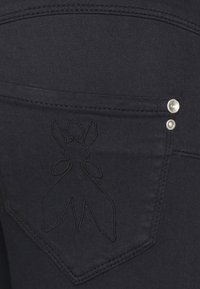 Czarne dżinsy mają dwa kieszeniowe zapięcia oraz ozdobnie haftowanego motyla na tylnej kieszeni i metalowe nity.