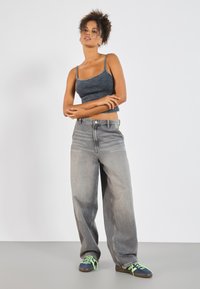 Crop top v tmavě modré žebrované tkanině s ramínky, v kombinaci se světle šedými kalhotami s širokými nohavicemi a modrými teniskami se zelenými tkaničkami.