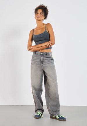 Korte top van donkerblauw rib stof met spaghettibandjes, gecombineerd met lichtgrijze wijde jeans en groen-geknoopte blauwe sneakers.