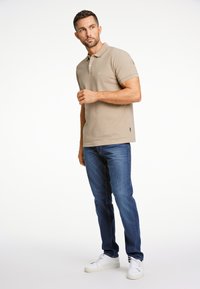 Beige pikétröja med texturerad yta, korta ärmar och en diskret logotyp. Matchad med blå jeans och vita sneakers.