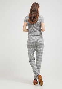 Jumpsuit stampato in bianco e nero con un motivo geometrico. Maniche corte, vita elasticizzata, gambe affusolate, abbinato a sandali con tacco alto.