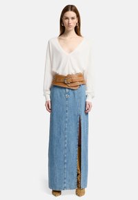Maglione bianco a V, gonna di jeans azzurro chiaro con uno spacco laterale e una cintura larga marrone con borchie. Scarpe a tacco quadro marroni con ritagli.