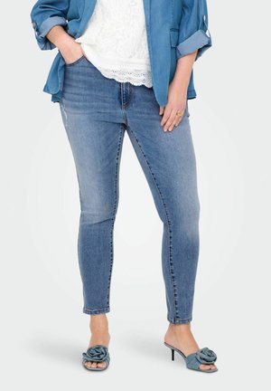 Jeans skinny de color azul claro hechos de mezclilla con cintura de tiro medio. Combinados con sandalias de tacón abierto que presentan un acento de flor.