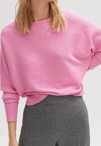 Pull rose côtelé à coupe ample et manches longues, associé à un pantalon taille haute à carreaux noir et blanc. Texture lisse.