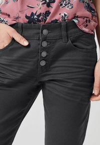 Pantalons noirs de longueur cheville en mélange de coton. Présentent une taille haute, cinq poches et trois boutons décoratifs à l'avant.