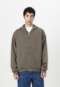 Olive green zip-up hoodie with a drawstring hood, ribbed cuffs, and hem; oversized fit, made of soft cotton material.