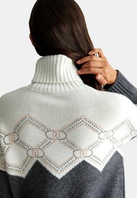 Maglione a collo alto lavorato a maglia in crema e grigio scuro. Presenta un motivo geometrico in fili d'argento e arancio sulle spalle. Tessuto testurizzato.
