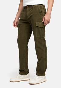 Olivengrønne fløjls cargo bukser med store sidelommer, tilpasset pasform og knaplukning. Stylet med hvide sneakers for kontrast.