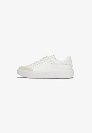 Lage, witte sneaker met een dikke zool, vetersluiting aan de voorkant en een beige suède neuskapdetail op een witte achtergrond.